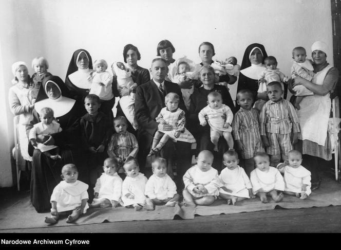 Fotografia grupowa dzieci i opiekunek z fundatorem żłobka Kazimierzem Rosnerem. Widoczna m.in. kierowniczka żłobka pani Sozańska (siedzi obok K. Rosnera); 1921-1939 r.