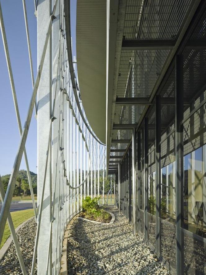 Przestrzeń między ścianą budynku Cairns Institute a stalową, ażurową elewacją zewnętrzną 