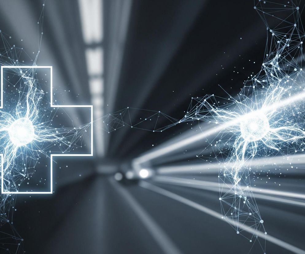 Na ciemnym tle z rozmazanymi, białymi smugami świetlnymi, przypominającymi tunel lub szybki ruch, widoczne są dwie połówki złożonej struktury. Po lewej stronie, w centrum, znajduje się jasnoniebieski świetlny symbol krzyża, wewnątrz którego pulsuje intensywne, błękitne światło, otoczone siecią połączonych punktów i linii, przypominających połączenia neuronowe lub sieć danych. Po prawej stronie, w podobnej odległości od centrum, znajduje się kolejna kula jasnego światła, również otoczona gęstą siecią punktów i linii, która wydaje się emitować świetliste promienie w prawą stronę obrazu, kontynuując motyw świetlnych smug. Całość utrzymana jest w chłodnych odcieniach szarości, błękitu i bieli.