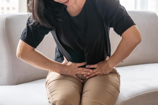 Kobieta z grymasem bólu trzyma się w okolicach brzucha