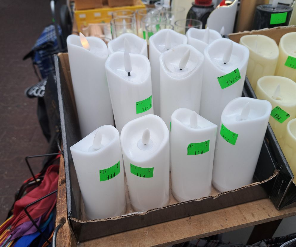 Białe i kremowe znicze LED z zielonymi naklejkami cenowymi, ułożone w kartonowych opakowaniach na drewnianej półce, sygnalizują problem z elektroodpadami, o którym przeczytasz na Super Biznes.