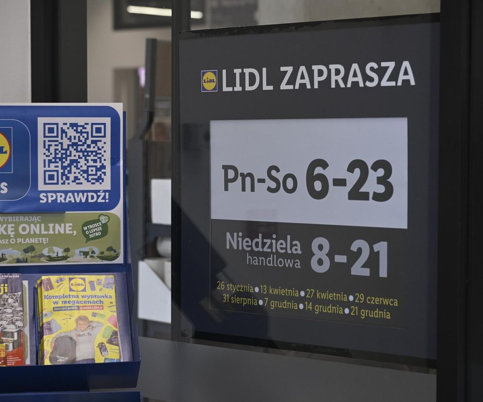 Znak informacyjny sklepu Lidl z godzinami otwarcia: od poniedziałku do soboty 6:00-23:00, w niedzielę handlową 8:00-21:00.  Wyświetlony kalendarz niedziel handlowych 2025 roku. Więcej informacji na temat niedziel handlowych znajdziesz na portalu Super Biznes.