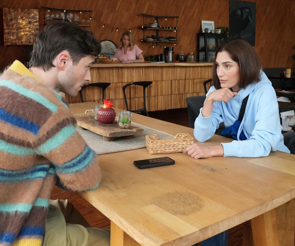 Orina Krajewska jako Celina i Marcel Opaliński jako Cezary siedzą przy drewnianym stole w kawiarni Feel Good. Celina, w jasnoniebieskiej bluzie, patrzy na Cezarego, który ubrany jest w kolorowy sweter. Rozmawiają o biżuterii Józefiny w Super Seriale.