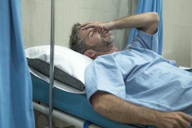 Zmartwiony mężczyzna leży na łóżku w sali szpitalnej. 