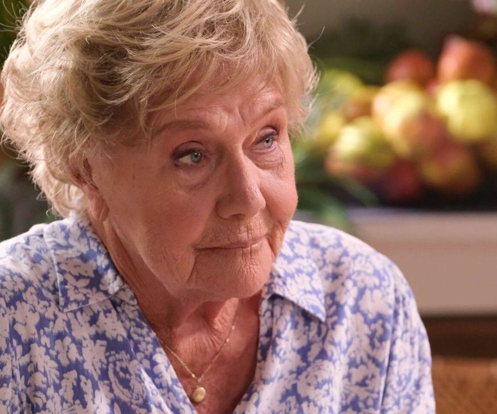 Barbara Mostowiak (Teresa Lipowska) w kwiecistej bluzce patrzy zamyślona, w tle rozmazane owoce. Zdjęcie ilustruje wzruszający moment w Grabinie z 1886 odcinka M jak miłość, o którym można przeczytać więcej na Super Seriale.