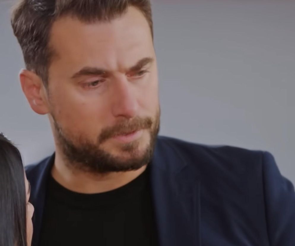 Kuzey z serialu Miłość i nadzieja z zamyśloną miną, ubrany w ciemną marynarkę i czarny t-shirt, w tle widoczna część ciemnych włosów Bahar. Obraz przedstawia ważny moment odcinka 328, gdzie Kuzey odkrywa kłamstwa żony. Więcej o losach bohaterów przeczytasz na Super Seriale.