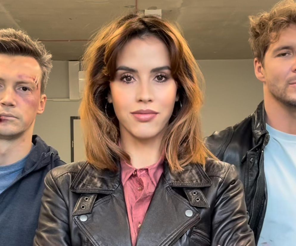 Aktorzy Krzysztof Kwiatkowski (Jakub Karski) i Mikołaj Roznerski (Marcin Chodakowski) z serialu „M jak miłość” z charakteryzacją imitującą pobicia, stojący obok aktorki Aleksandry Pałaty (Kama). Zdjęcie z planu serialu, zza kulis, zapowiadające dramatyczne sceny i nadchodzącą walkę. Więcej o ich losach przeczytasz na Super Seriale.