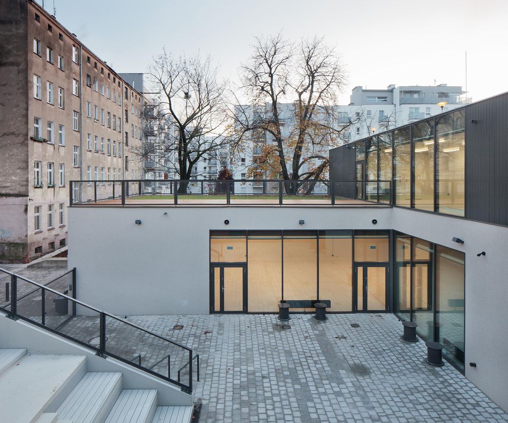 Zrewitalizowane podwórze z Centrum Aktywności Lokalnej na Przedmieściu Oławskim. Widoczne nowoczesne schody, patio z kostki brukowej, duże przeszklone ściany i zielony taras. Projekt autorstwa CH+ architekci, jeden z TOP60 konkursu Życie w Architekturze 2025 na portalu Architektura Murator Plus.