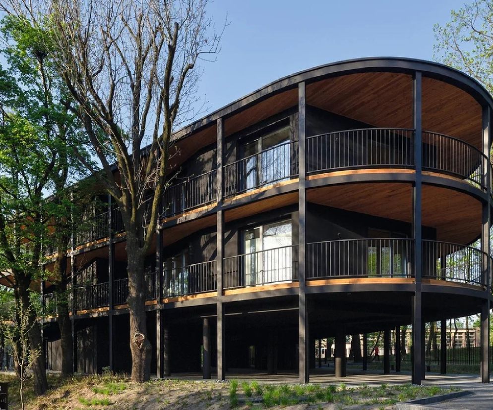 Nowoczesny budynek Villa Reden z falistymi, czarnymi balkonami i drewnianymi podbitkami, wsparty na słupach, otoczony zielenią drzew. O architekturze Macieja Franty i innych inspirujących projektach przeczytasz na portalu Architektura Murator Plus.