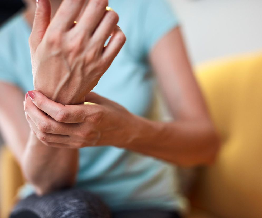 Kobieta masuje bolący nadgarstek, co symbolizuje dolegliwości stawów przy RZS. Regularne ćwiczenia fizyczne i fizjoterapia są kluczowe w zarządzaniu objawami RZS. Więcej o metodach leczenia i zapobiegania bólowi stawów przeczytasz na Poradnik Zdrowie.