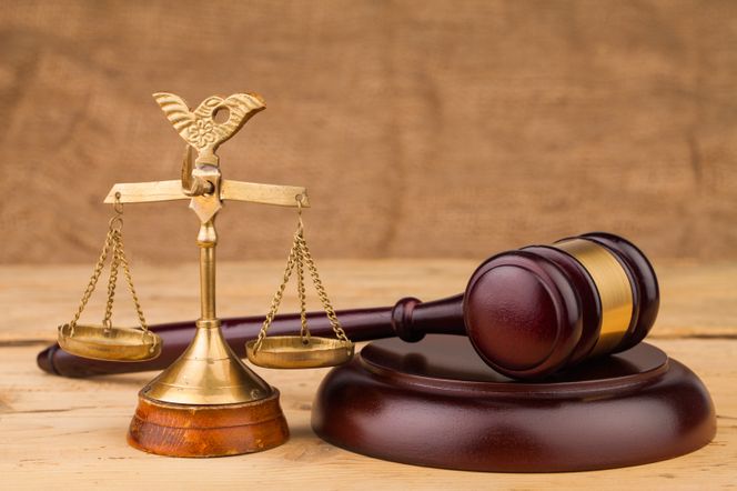 Drewniany młotek sędziowski leżący obok złotych wag symbolizujących sprawiedliwość na tle drewnianego stołu, co odnosi się do decyzji sądu w sprawie Henryka Kani. Więcej o prawie i biznesie przeczytasz na portalu Super Biznes.