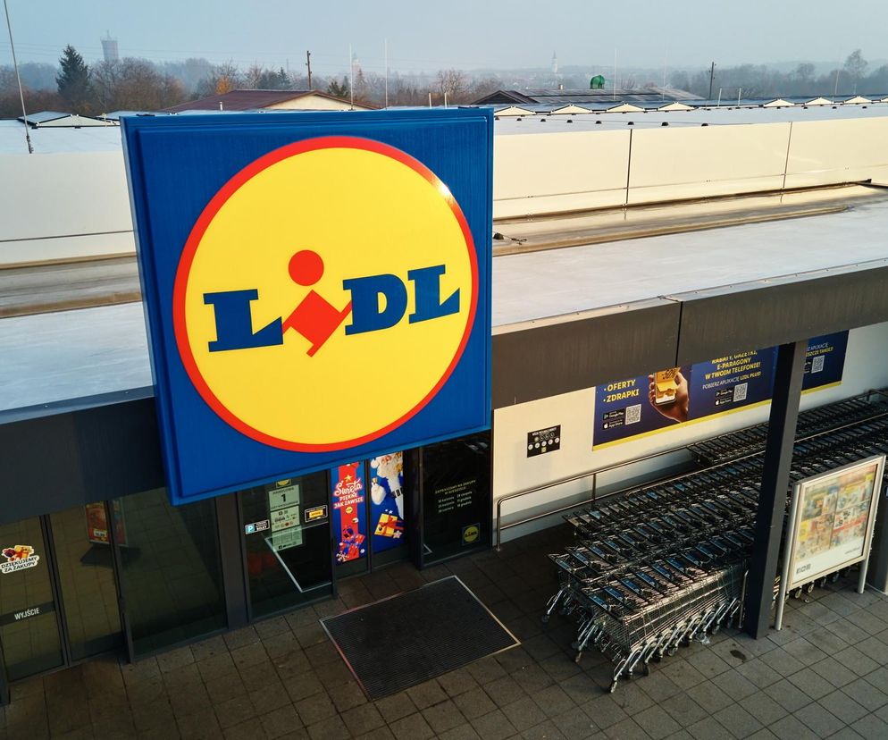 Zewnętrzny widok na sklep Lidl z dużym, niebiesko-żółtym logo. Przed wejściem widoczne są stosy wózków zakupowych oraz plakaty informujące o aktualnych promocjach. To właśnie tu klienci znajdą kuchenne hity, takie jak markowe frytkownice i żeliwne naczynia, o których więcej przeczytasz na portalu Super Biznes.