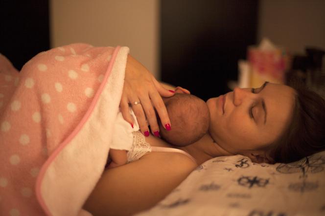 kobieta leżąca w łóżku z noworodkiem na piersi