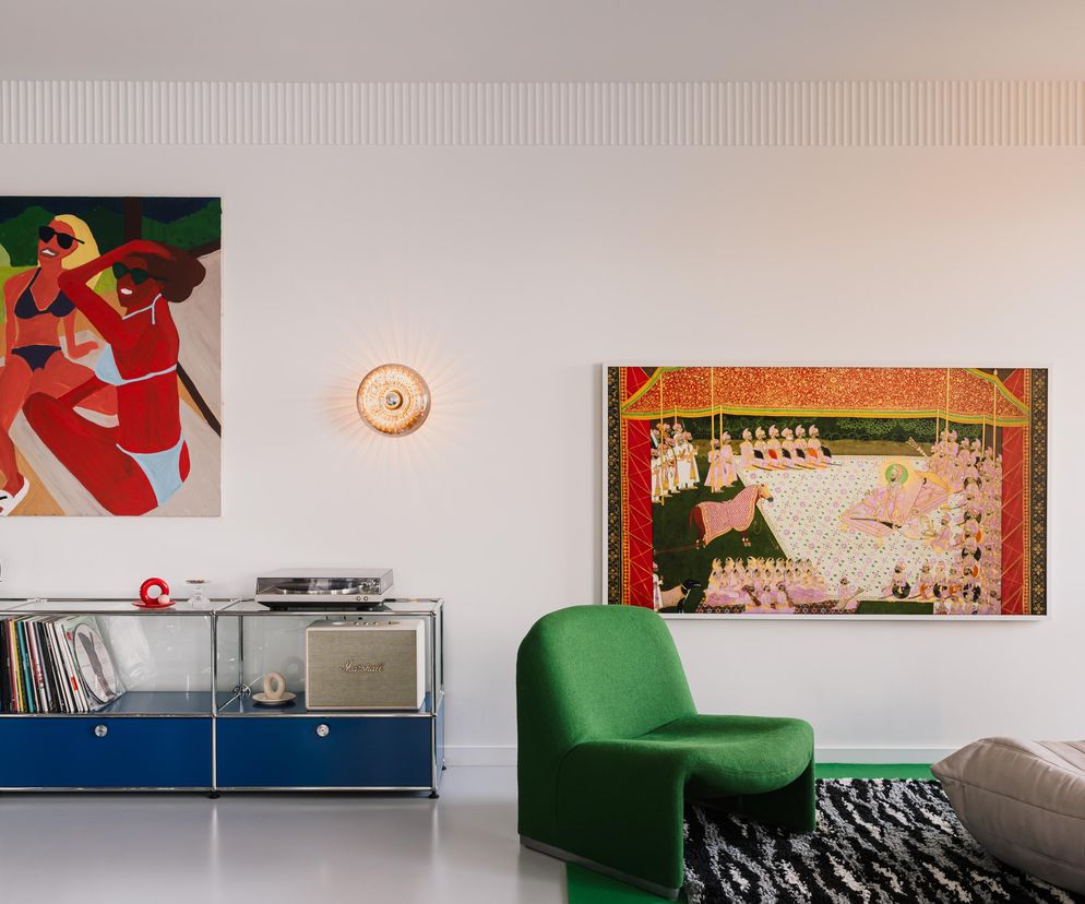 Nowoczesne wnętrze apartamentu w Tychach z ikonicznym designem, gdzie widoczny jest niebieski regał USM Haller z płytami winylowymi, beżowa sofa Togo oraz zielony fotel Alky. Na ścianie obrazy Michała Żytniaka i grafika zainspirowana Amy Victorią Marsh, o której przeczytasz więcej na Architektura Murator Plus.