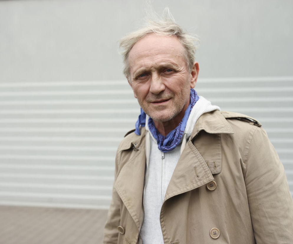 Aktor Andrzej Chyra w beżowym płaszczu i z niebieską chustą na szyi. O jego metamorfozie przeczytasz w serwisie Eska.