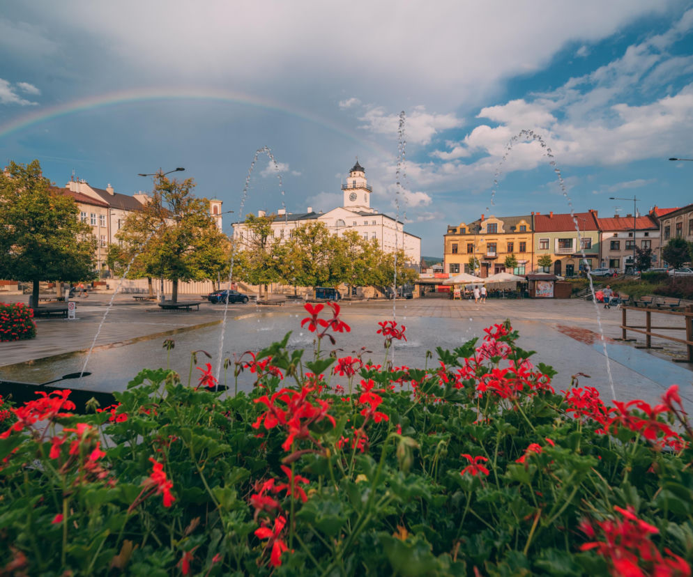 Rynek w Gorlicach z fontanną, ratuszem i tęczą na niebie. O zabytkach małopolskiego miasta przeczytasz na Eska Kraków.