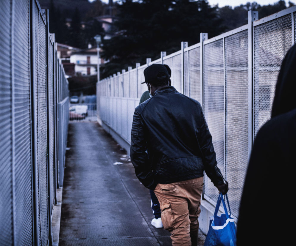 Mężczyzna z torbą idzie wzdłuż wysokiego metalowego ogrodzenia. O planach walki z migracją przeczytasz na Eska.