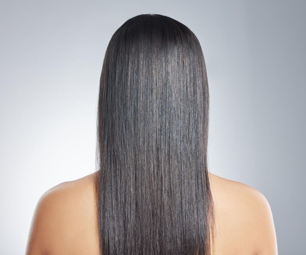 Gładkie, lśniące czarne włosy kobiety widziane z tyłu. O tym, jak uzyskać efekt glass hair, przeczytasz na PZ Uroda.