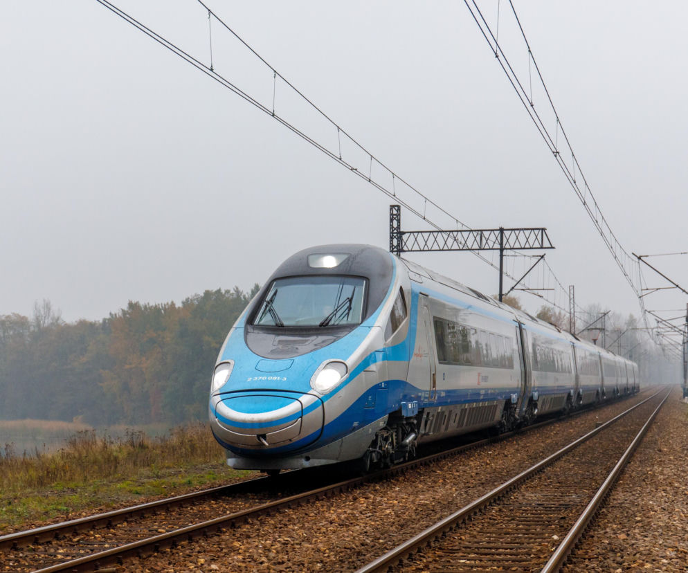 Srebrno-niebieski pociąg ekspresowy pędzi po torach wśród jesiennych drzew. O planach szybkich połączeń czytaj w Eska Szczecin.