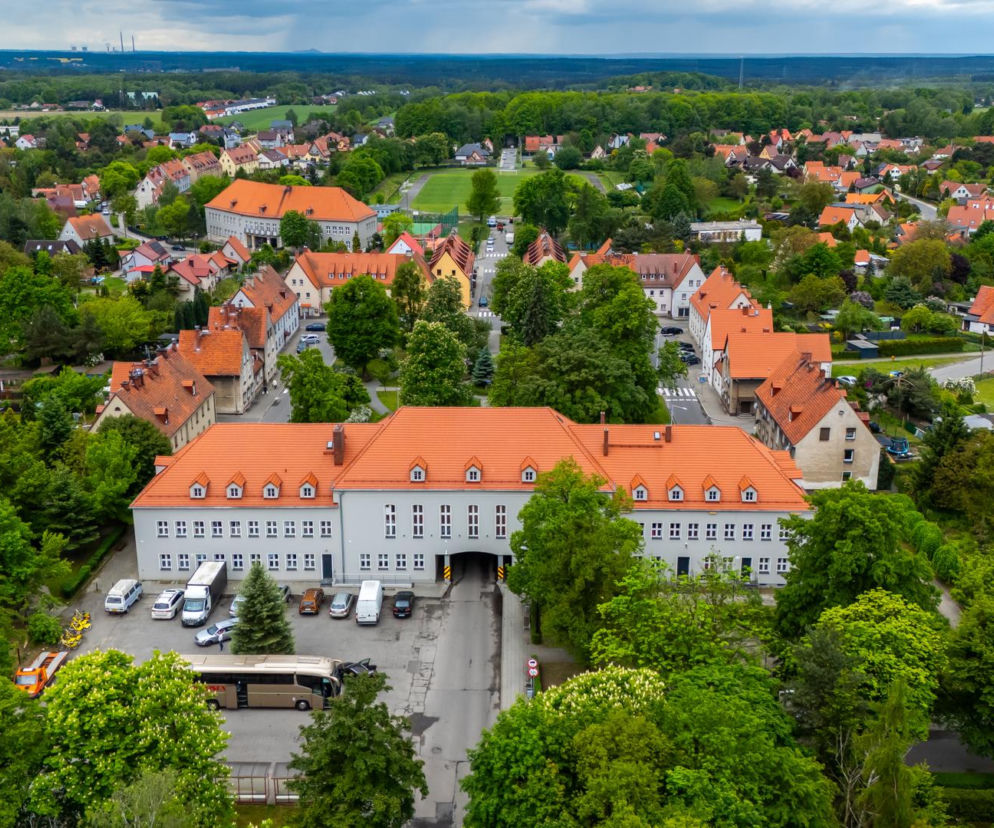 Osiedle Wilcze Gardło w Gliwicach z lotu ptaka, z głównym budynkiem z pomarańczowym dachem i licznymi, otoczonymi zielenią domami jednorodzinnymi. Ten ambitny projekt urbanistyczny III Rzeszy, dziś cenny zabytek architektury, przedstawia miasto-ogród z niską zabudową i spójnym stylem, o czym więcej przeczytasz na Architektura Murator Plus.