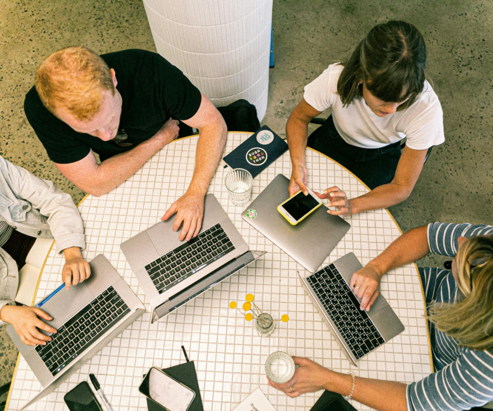 Cztery osoby siedzące przy stole, pracujące na laptopach i smartfonach, co symbolizuje dynamiczne środowisko startupowe. Ta scena podkreśla sukces polskich startupów, o czym więcej przeczytasz na Super Biznes.