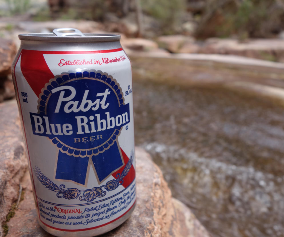 Otwarta puszka piwa Pabst Blue Ribbon na kamieniu przy strumieniu. O kradzieży 50 tys. puszek przeczytasz na Eska.