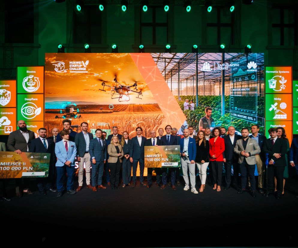 Uczestnicy gali Huawei Startup Challenge na scenie, wśród nich laureaci z czekami, na tle dużego ekranu przedstawiającego innowacje AgriTech: dron nad polem, uprawy w szklarni oraz loga startupów. Więcej o zwycięzcach przeczytasz na Super Biznes.