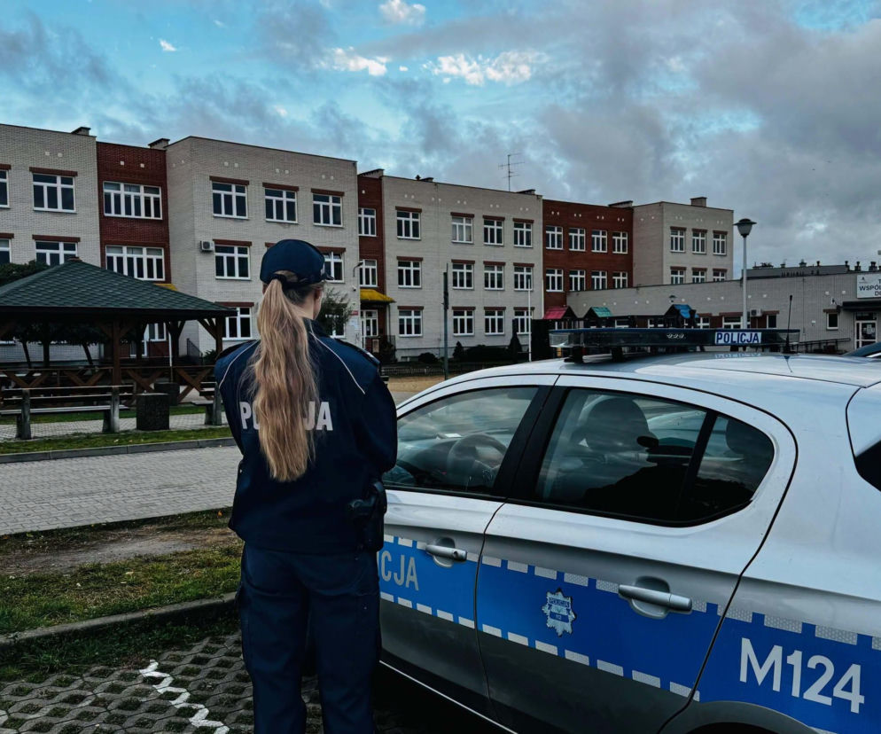 Policjantka przy radiowozie przed budynkiem szkoły. O wzmożonych kontrolach policji przeczytasz na SE Białystok.