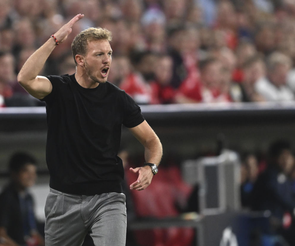 Julian Nagelsmann w czarnym t-shircie i szarych spodniach, z ekspresją na twarzy, gestykuluje rękami podczas meczu, instruując zawodników. W tle rozmazany tłum na trybunach. Więcej o emocjach na mundialu przeczytasz na naszym portalu.
