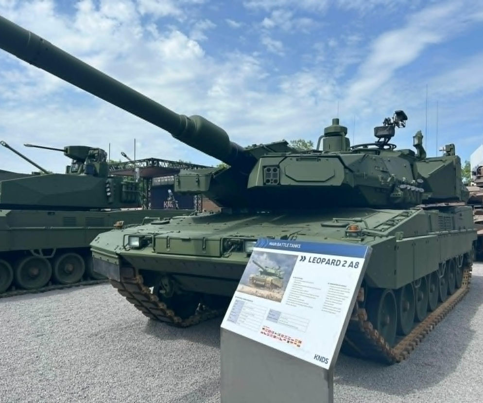 Nowoczesny czołg Leopard 2A8 w barwach NATO na tle nieba, z widoczną tablicą informacyjną prezentującą jego specyfikacje. To kluczowy element obronności omawiany na naszym portalu w kontekście porozumienia Niemiec i Francji ws. KNDS.