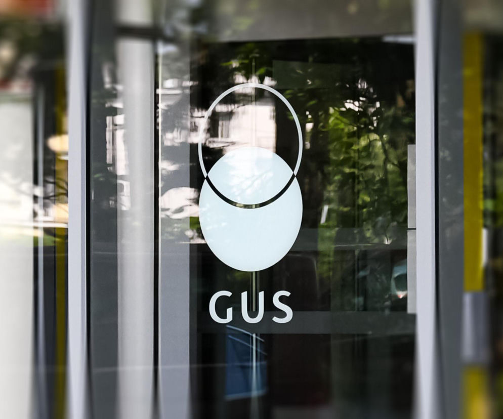 Białe logo GUS na szklanych drzwiach wejściowych. O najnowszej medianie wynagrodzeń przeczytasz na SE Superbiz.