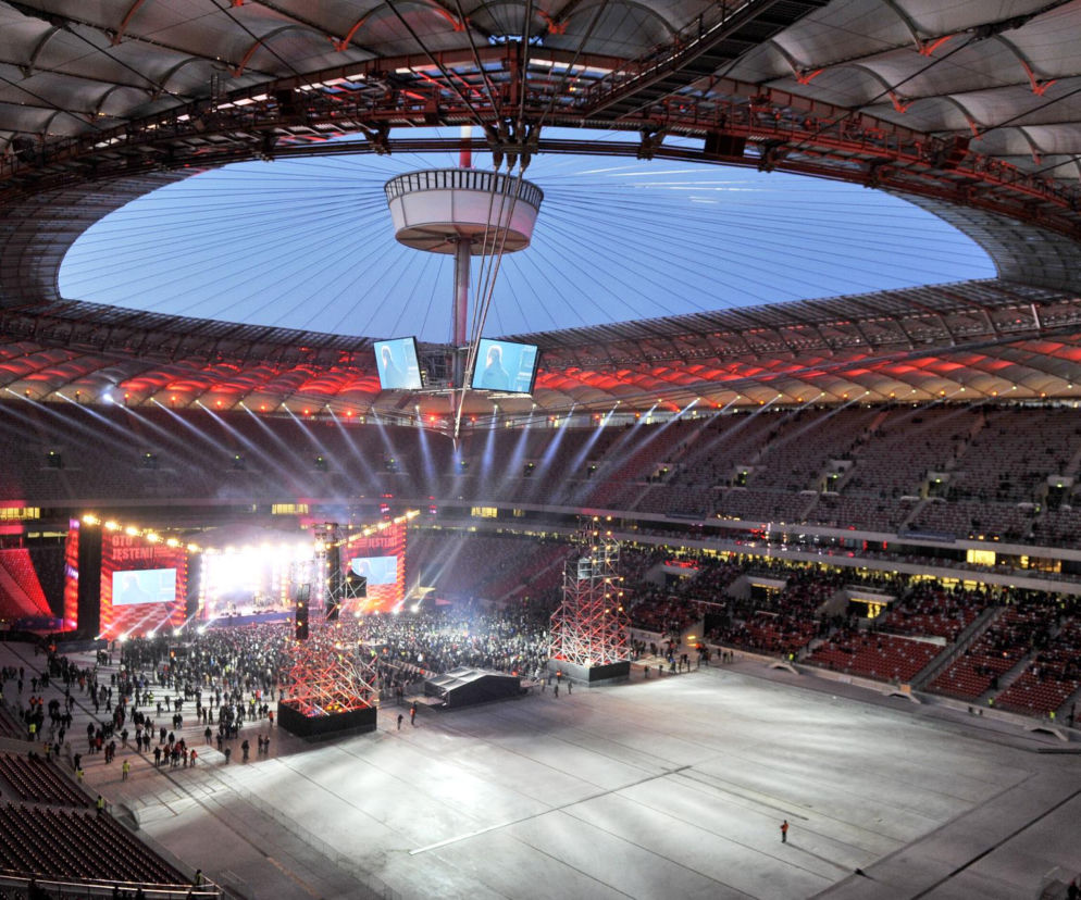 Oświetlony stadion PGE Narodowy z góry. Wewnątrz scena i tłum fanów. O zmianach w regulaminach koncertów przeczytasz w Eska.