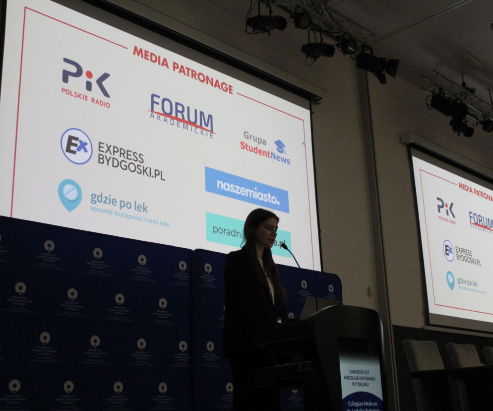 Młoda kobieta w czarnej marynarce przemawia z mównicy, prezentując slajd z logo patronów medialnych 46. Kongresu EPSA, w tym PoradnikZdrowie.pl. Tło stanowi ściana z logo Collegium Medicum UMK w Toruniu, co odzwierciedla podsumowanie kongresu w Bydgoszczy.