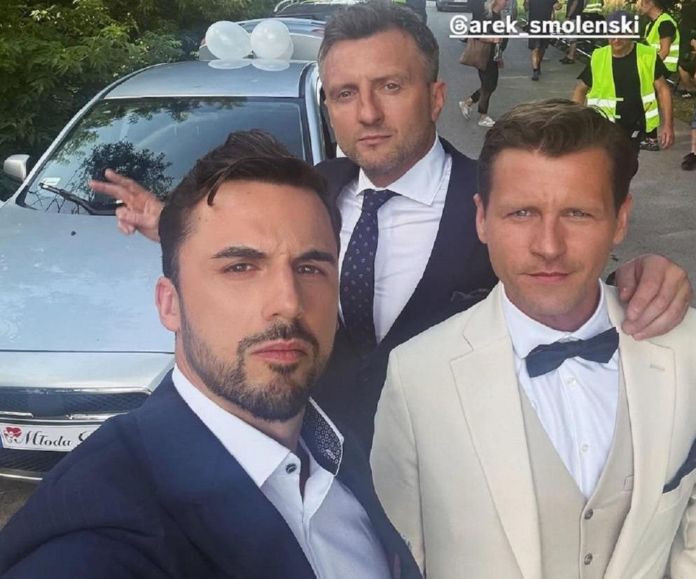 Trzej eleganccy mężczyźni w garniturach przed ślubnym autem. O kulisach wesela w M jak miłość przeczytasz na Eska.