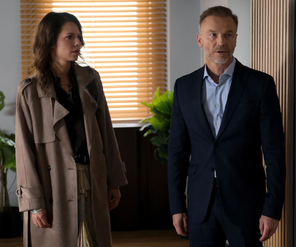 Maria Wieczorek jako Paulina Lipska i Krystian Wieczorek jako Andrzej Budzyński patrzą na siebie z troską. Maria ma na sobie beżowy płaszcz i ciemną bluzkę, a Krystian granatowy garnitur i jasną koszulę. Więcej o ich losach w Super Seriale.