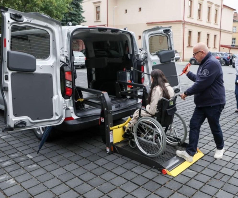 Mężczyzna pomaga kobiecie na wózku wjechać windą do auta. O usłudze Taxi Help przeczytasz na Eska Tarnów.