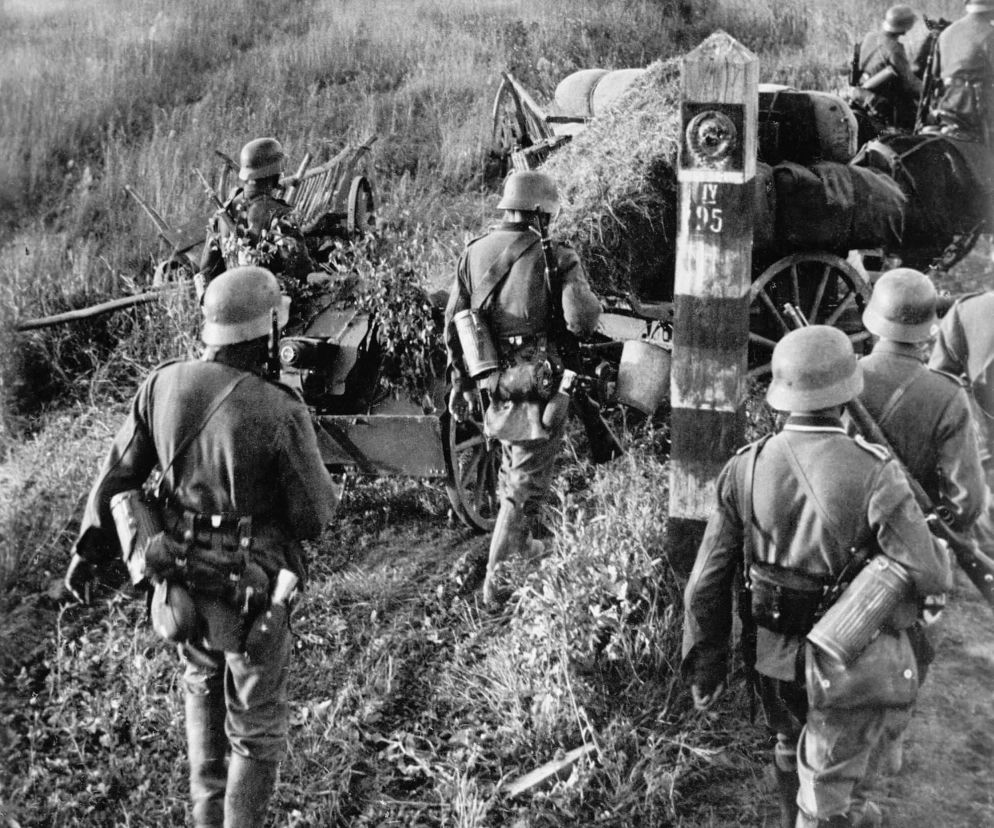 Żołnierze Wehrmachtu maszerujący wiejską drogą podczas operacji Barbarossa, obok słupa granicznego z oznaczeniem IV 95, co symbolizuje początek inwazji na ZSRR w 1941 roku. Więcej o tym konflikcie przeczytasz na naszym portalu.