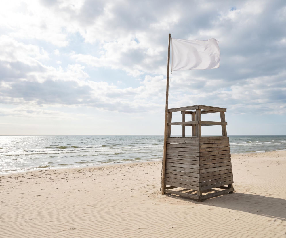 Drewniana wieża ratownika z białą flagą na pustej plaży. O bezpiecznej kąpieli w Świnoujściu przeczytasz na SE Szczecin.