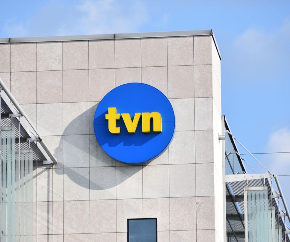 Logo TVN w kolorach żółtym i niebieskim na tle jasnej, kafelkowanej ściany budynku, symbolizujące medialne zmiany. O przyszłości stacji i planowanych zwolnieniach w branży medialnej przeczytasz na Super Biznes.