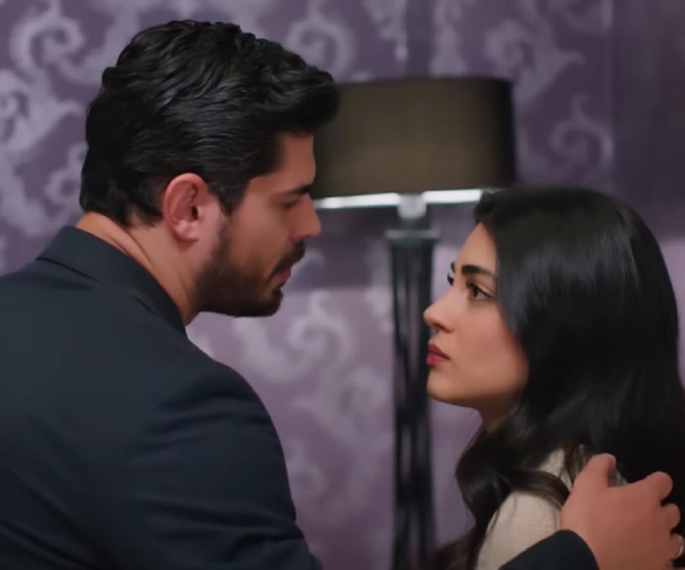 Cihan, mężczyzna o ciemnych włosach i brodzie, spogląda na Hancer, kobietę o długich, ciemnych włosach, w eleganckim wnętrzu z tapetą w fioletowe wzory. Oboje patrzą na siebie z powagą. Ta scena z pewnością wywoła wiele emocji, o czym możesz przeczytać na Super Seriale.