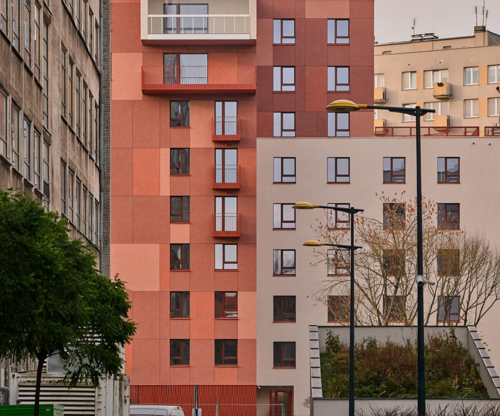 Nowoczesny budynek Korso Mińska 17 na warszawskim Kamionku o elewacji z tynków w odcieniach cegły, z balkonami i loggią, w otoczeniu zieleni. Projekt Latergrupa Architekci nawiązuje do historycznego charakteru dzielnicy, o czym przeczytasz na Architektura Murator Plus.