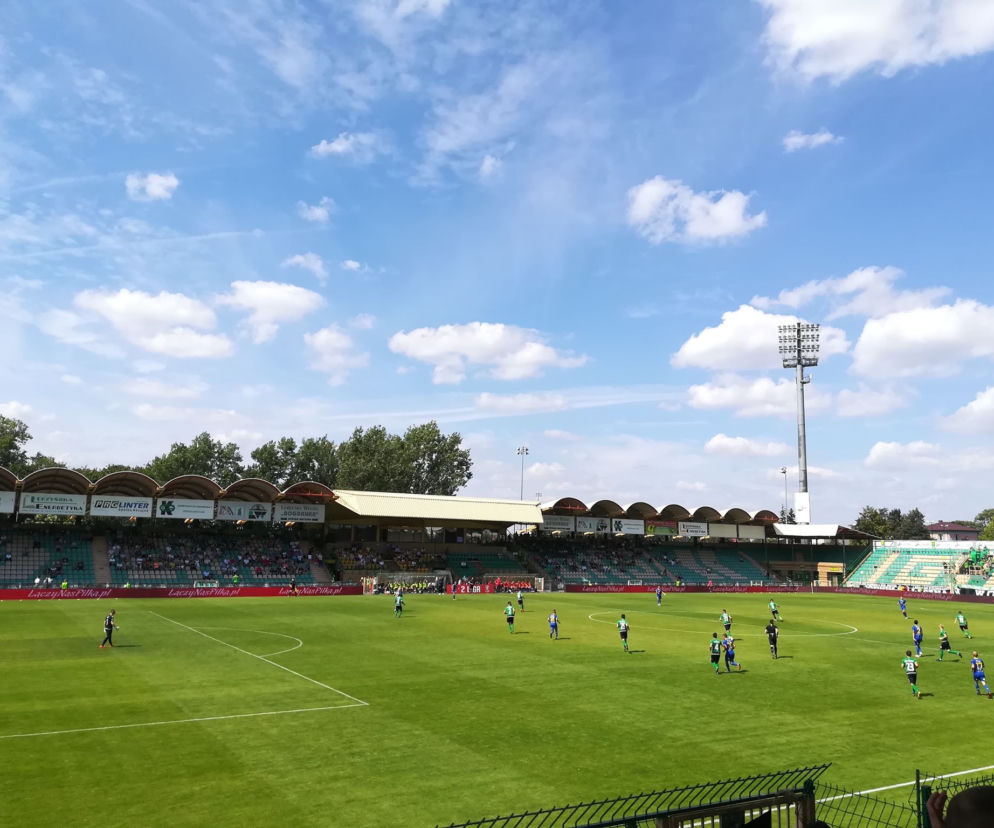 Piłkarze grają mecz na zielonej murawie stadionu przy licznej widowni. O transmisjach na PZPN+ przeczytasz na SE Supersport.