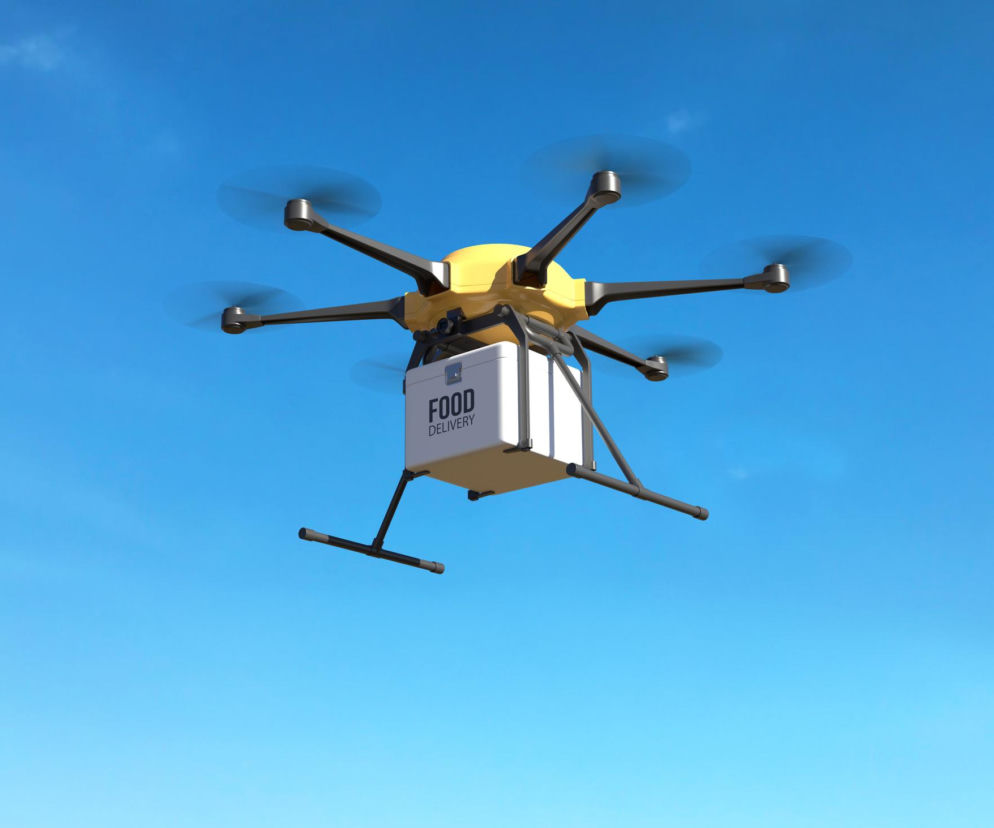 Dron transportuje białe pudełko z napisem FOOD DELIVERY na tle nieba. O przemycie do więzienia przeczytasz na Eska.
