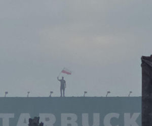 Mężczyzna z flagą na dachu kamienicy. Symboliczny kadr z Godziny W