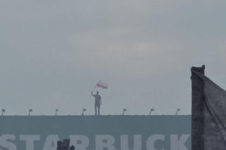Mężczyzna z flagą na dachu kamienicy. Symboliczny kadr z Godziny W
