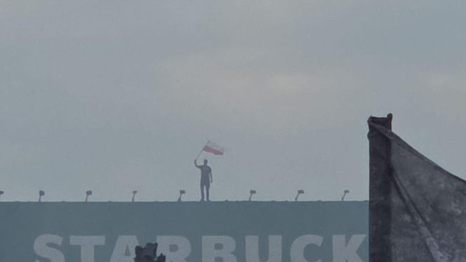 Mężczyzna z flagą na dachu kamienicy. Symboliczny kadr z Godziny W