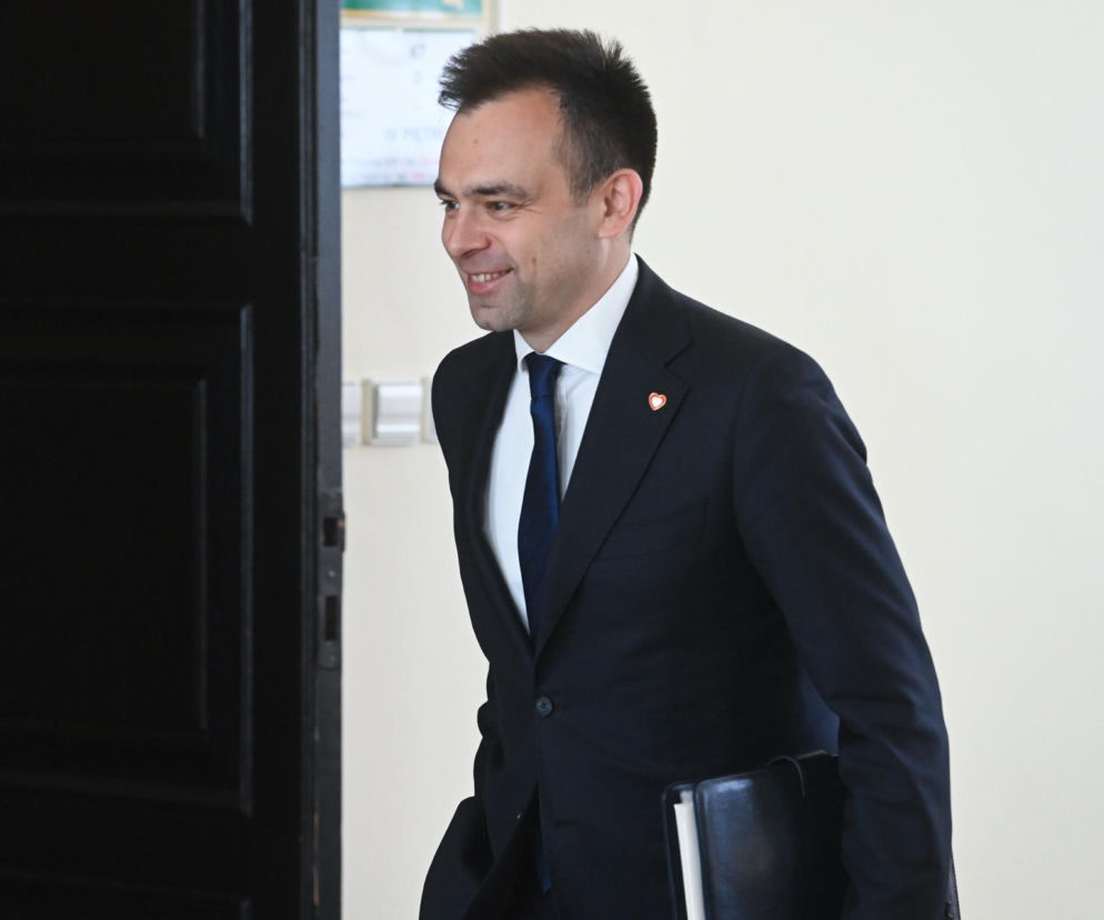 Minister Finansów Andrzej Domański w garniturze z uśmiechem wychodzi z pokoju, trzymając teczkę. Na klapie marynarki przypinka w kształcie serca. Informacje o majątku ministra przeczytasz na Super Biznes.