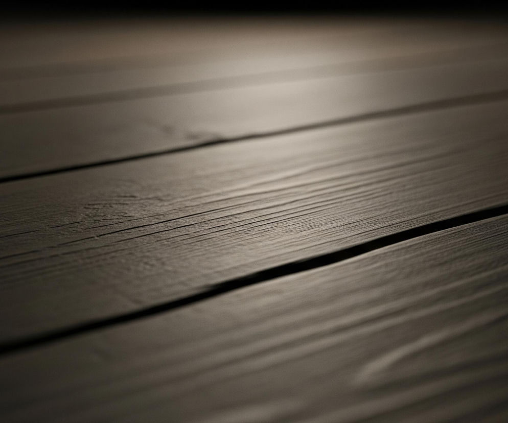 Ciemne, drewniane deski ułożone równolegle do siebie wypełniają kadr. Powierzchnia desek jest chropowata, z wyraźnie widocznym usłojeniem drewna. Światło pada z górnej części obrazu, tworząc jasną, rozmazaną plamę na deskach, która stopniowo przechodzi w ciemniejsze odcienie brązu i szarości.