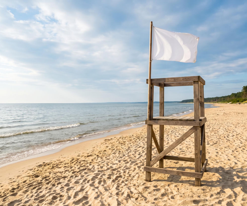 Drewniana wieża ratownika z białą flagą na pustej plaży w Pogorzelicy. O warunkach nad morzem przeczytasz na SE Szczecin.
