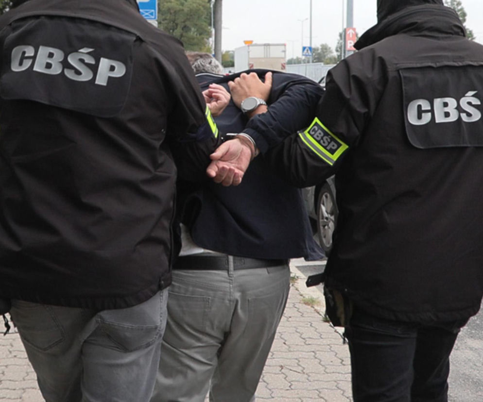 Dwaj funkcjonariusze CBŚP prowadzą zatrzymanego mężczyznę w kajdankach. O akcji w Żorach przeczytasz na SE.